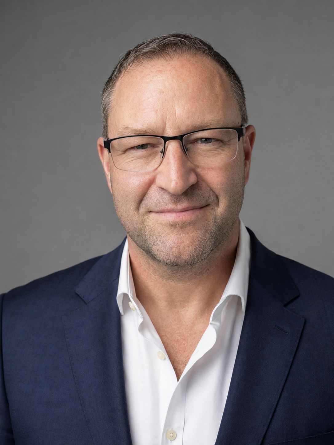Forrest Andrew Jones, Chief Investment Officer at Blackwater Investment Group Inc., in a navy jacket and open-collar white shirt against a plain grey studio background.